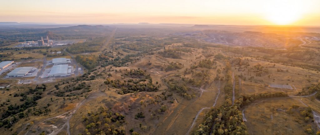 Aerial view at sunset of a post-mining landscape: a logistics estate and gas-fired power station on rehabilitated land, with an open-cut mine beyond